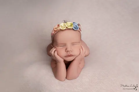 Новородено подпира брадичка с двете си ръчички, с лентичка от пъстри сатенени рози