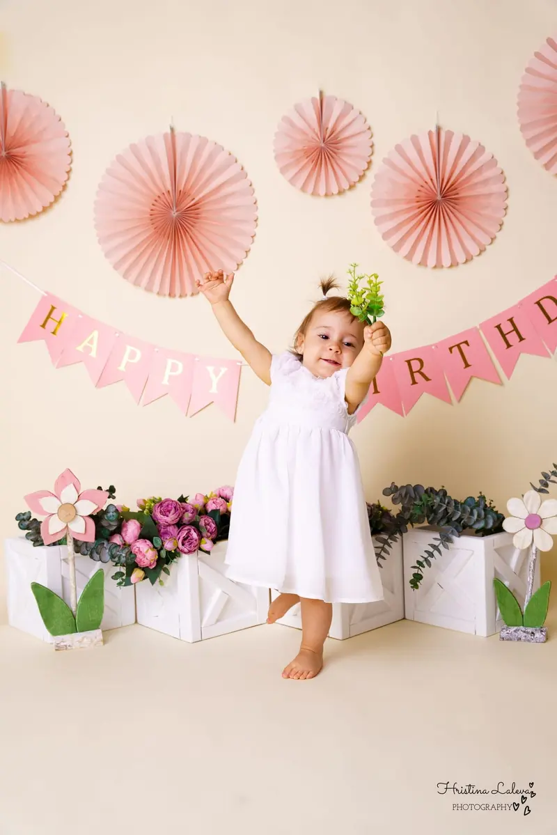 Танцуващо момиченце в бяла рокля вдига ръце под розов надпис Happy Birthday
