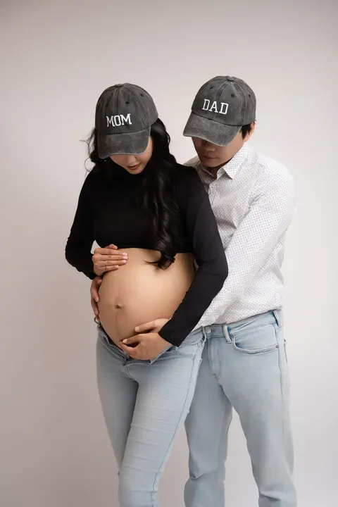 Бъдещите мама и татко с шапки „MOM“ и „DAD“ гледат заедно към корема