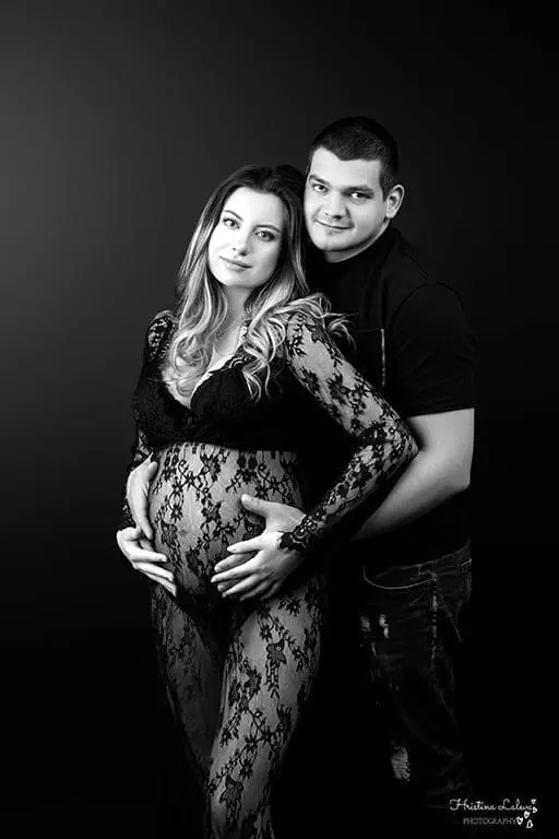 Черно-бял портрет на двойка в очакване: тя в черна дантела, той я прегръща отзад с ръце върху коремчето