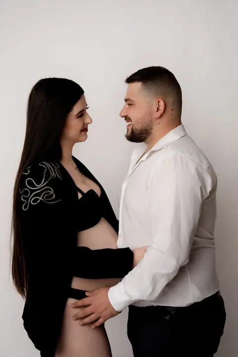 Бъдещите родители се гледат усмихнати, той в бяла риза с ръка на корема ѝ