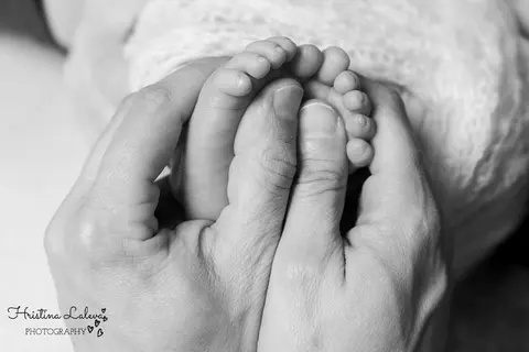 Мъничките крачета на бебето в ръцете на възрастен, до плетено одеялце, черно-бяло