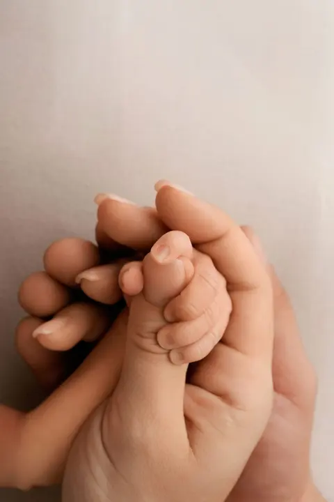 Мъничката ръчичка на бебето стиска пръста на родителя си