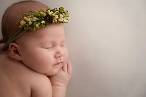 Спящо бебе с венче от сухи треви и мънички шишарки, с ръчичка под брадичката