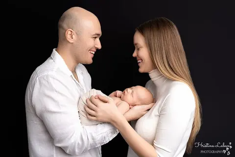 Щастливи родители в бяло държат новороденото между себе си на черен фон
